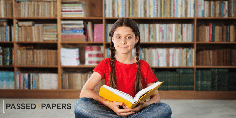 Girl sitting with book in front of book shelf. Verbal Reasoining Independent School Exam